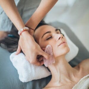 A woman relaxes during a gua sha facial massage at a spa, promoting wellness and beauty.